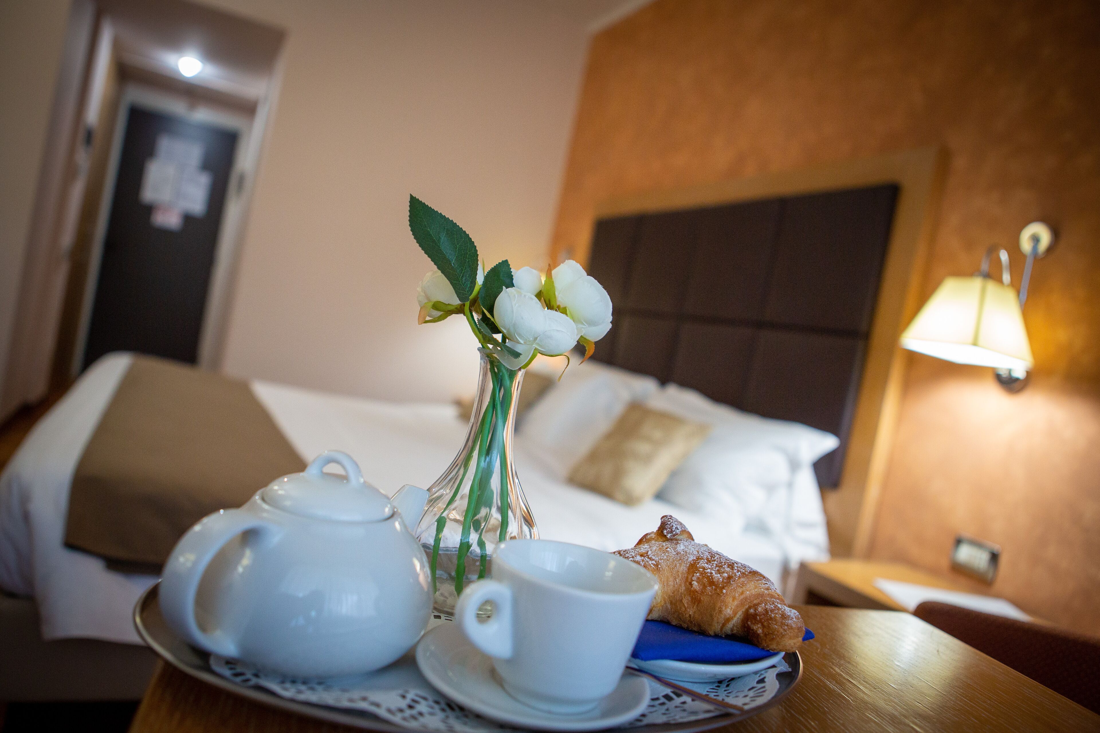 A neatly arranged breakfast tray with a teapot, cup, and pastry on a table in a hotel room.