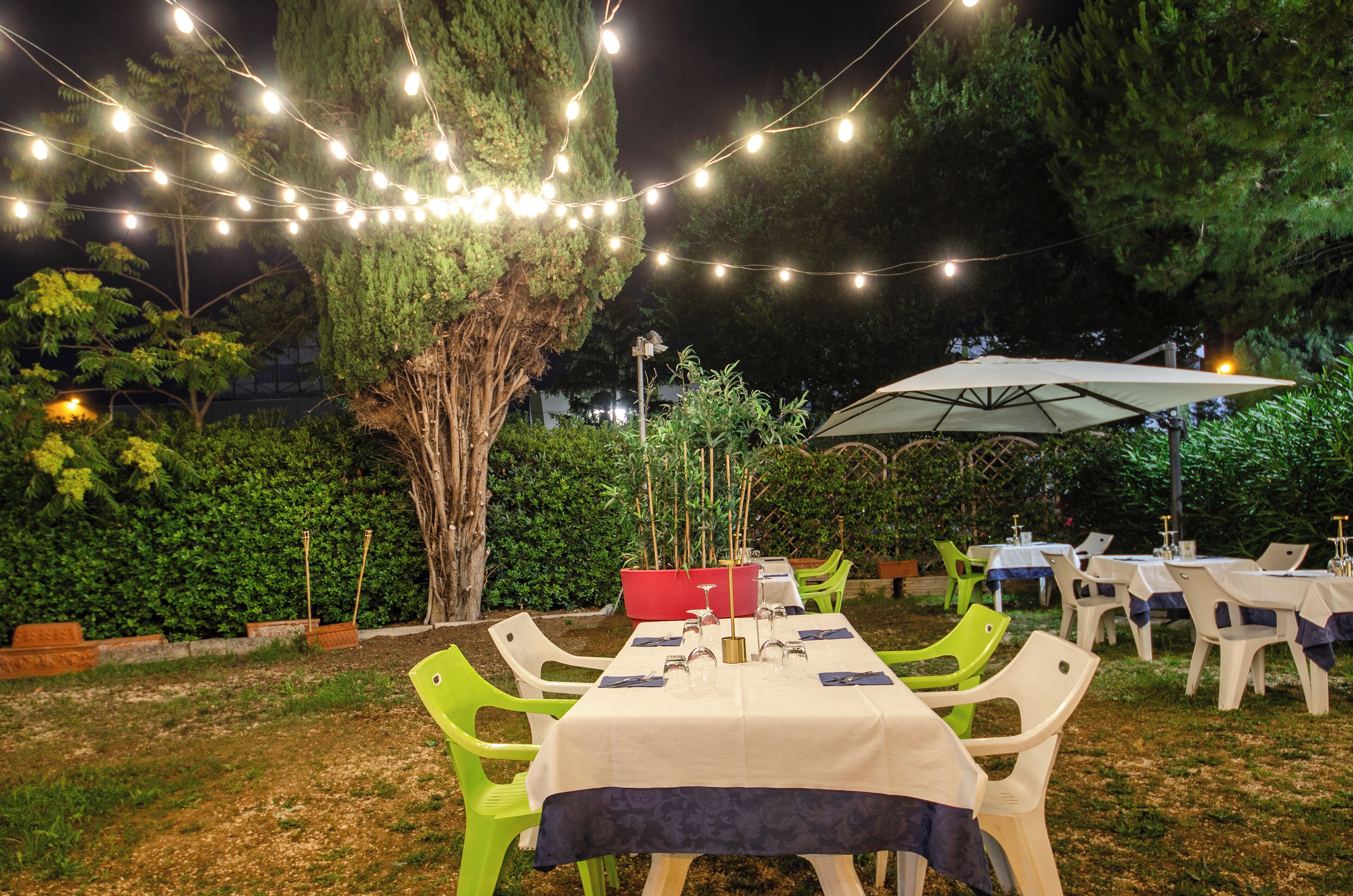 An outdoor dining area with string lights, tables with white tablecloths, and green chairs.