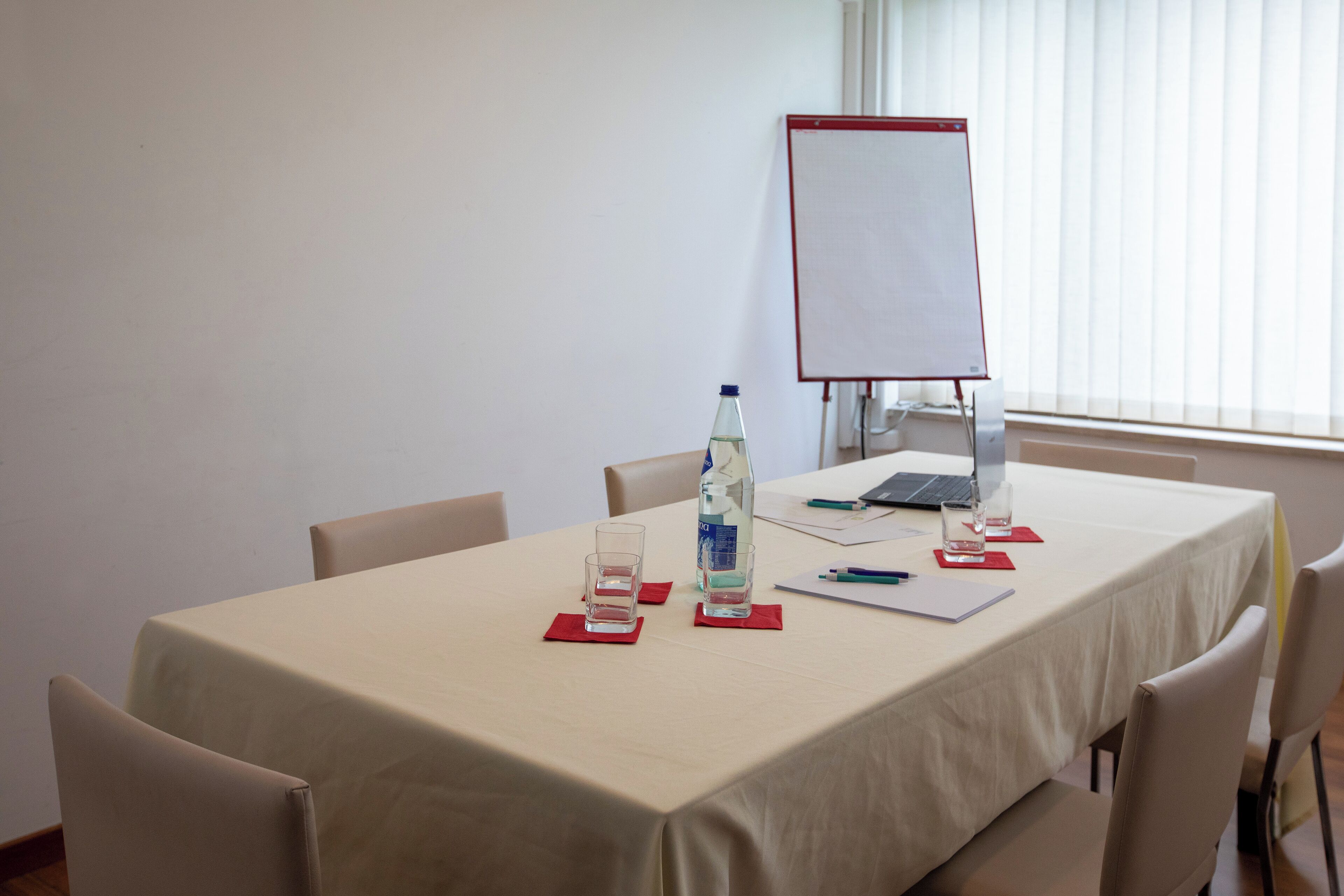 A conference room with a table set for a meeting, a laptop, a flip chart, and water bottles.