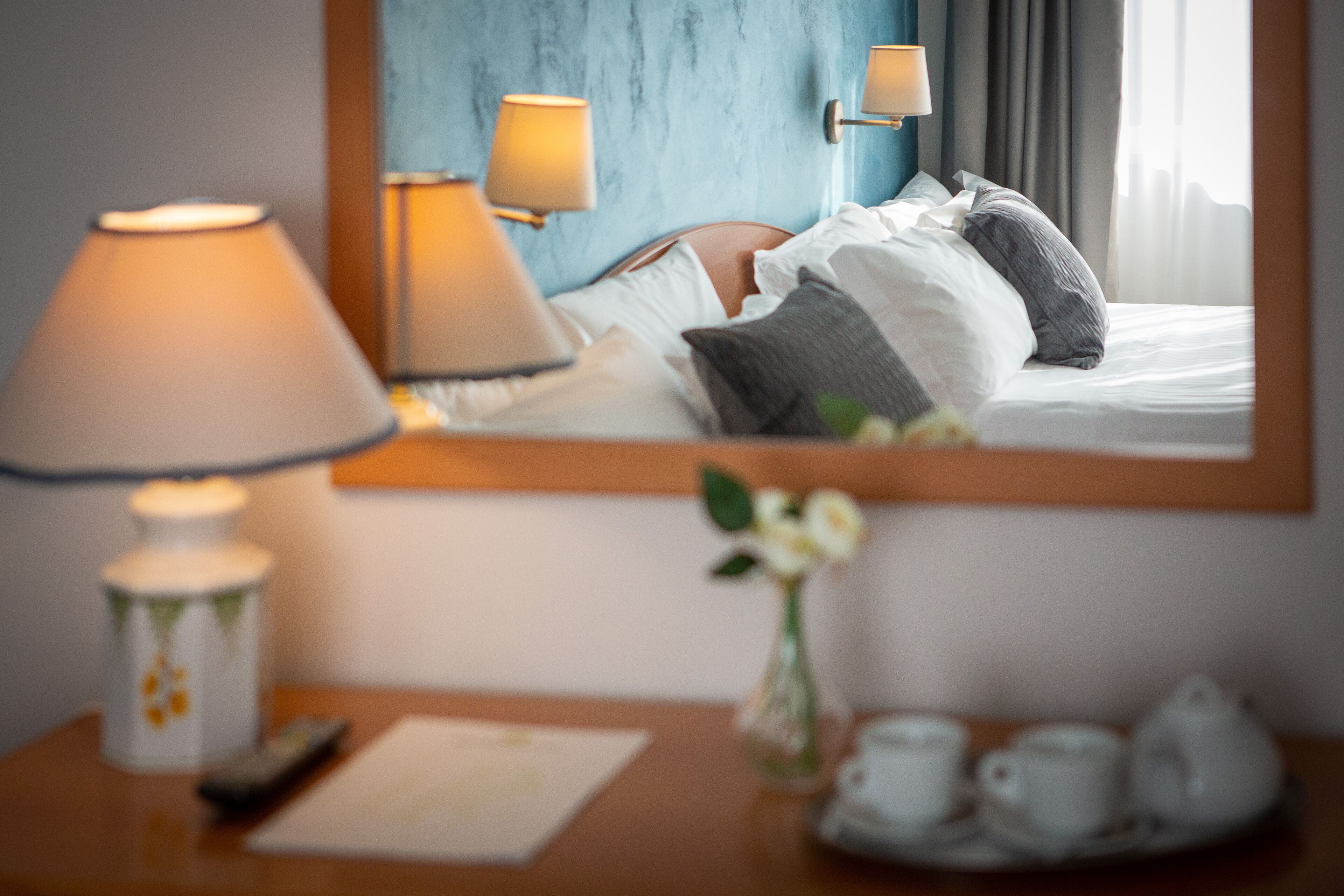 Una habitación de hotel con una cama, lámparas de noche, un jarrón con flores, un control remoto y una bandeja con tazas de té.