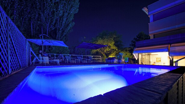 Ein Nacht-Pool mit blauer Beleuchtung, umgeben von Liegestühlen und Sonnenschirmen.
