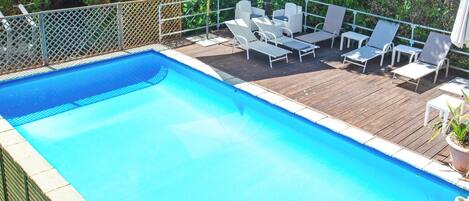 A rectangular swimming pool with a wooden deck and white lounge chairs.