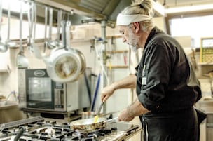 Una persona cocinando en una cocina profesional con electrodomésticos y utensilios de acero inoxidable.