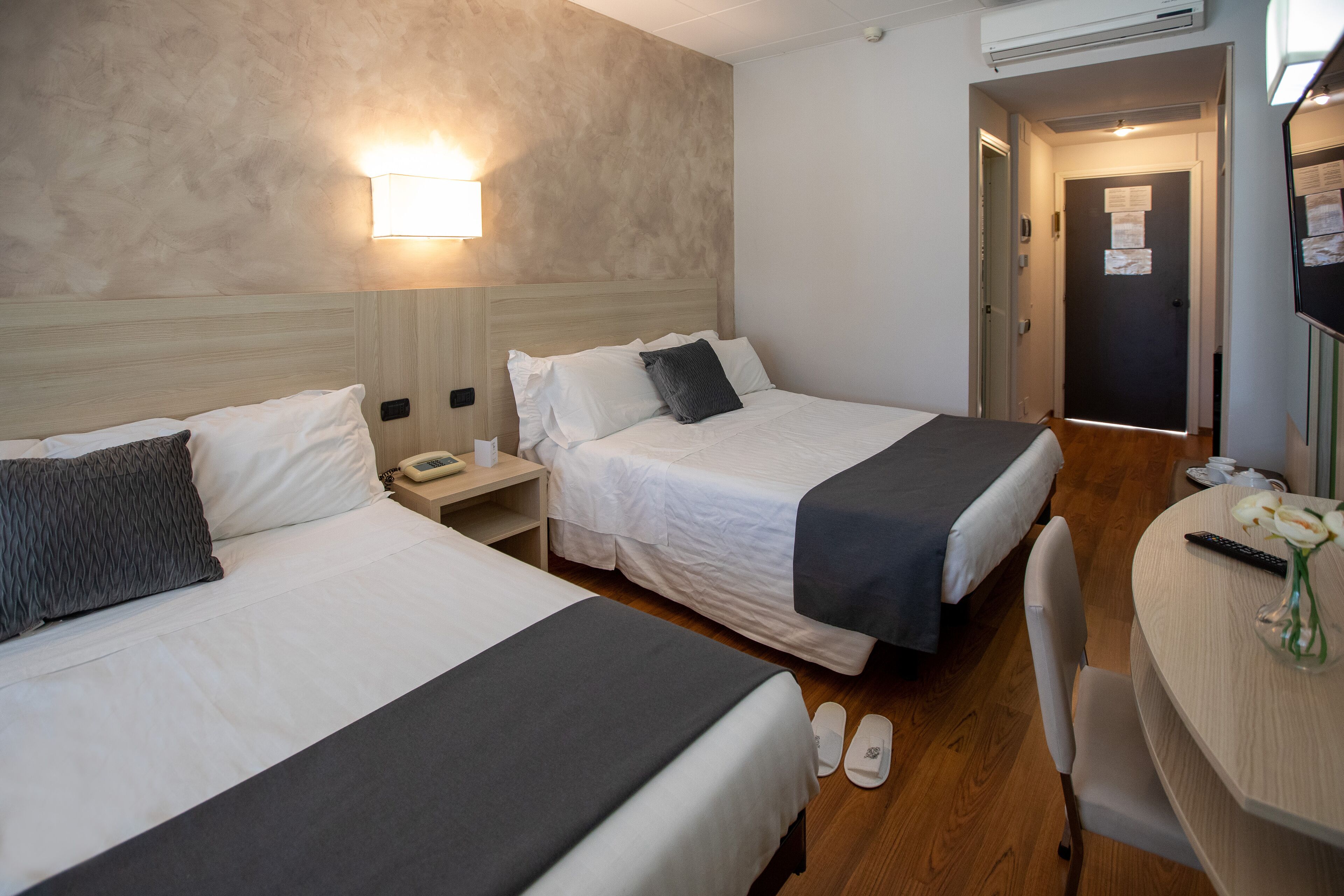 A hotel room with two beds, a desk, and a chair. There is a nightstand with a phone and a lamp.
