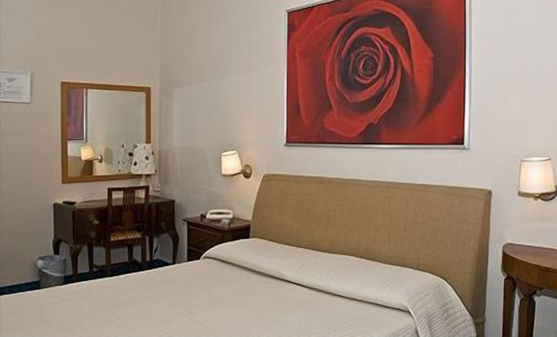 A hotel room with a bed, a desk, a chair, a telephone, and a wall-mounted lamp.