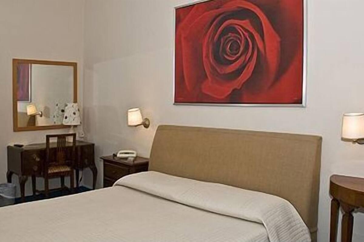 A hotel room with a bed, a desk, a chair, a telephone, and a wall-mounted lamp.