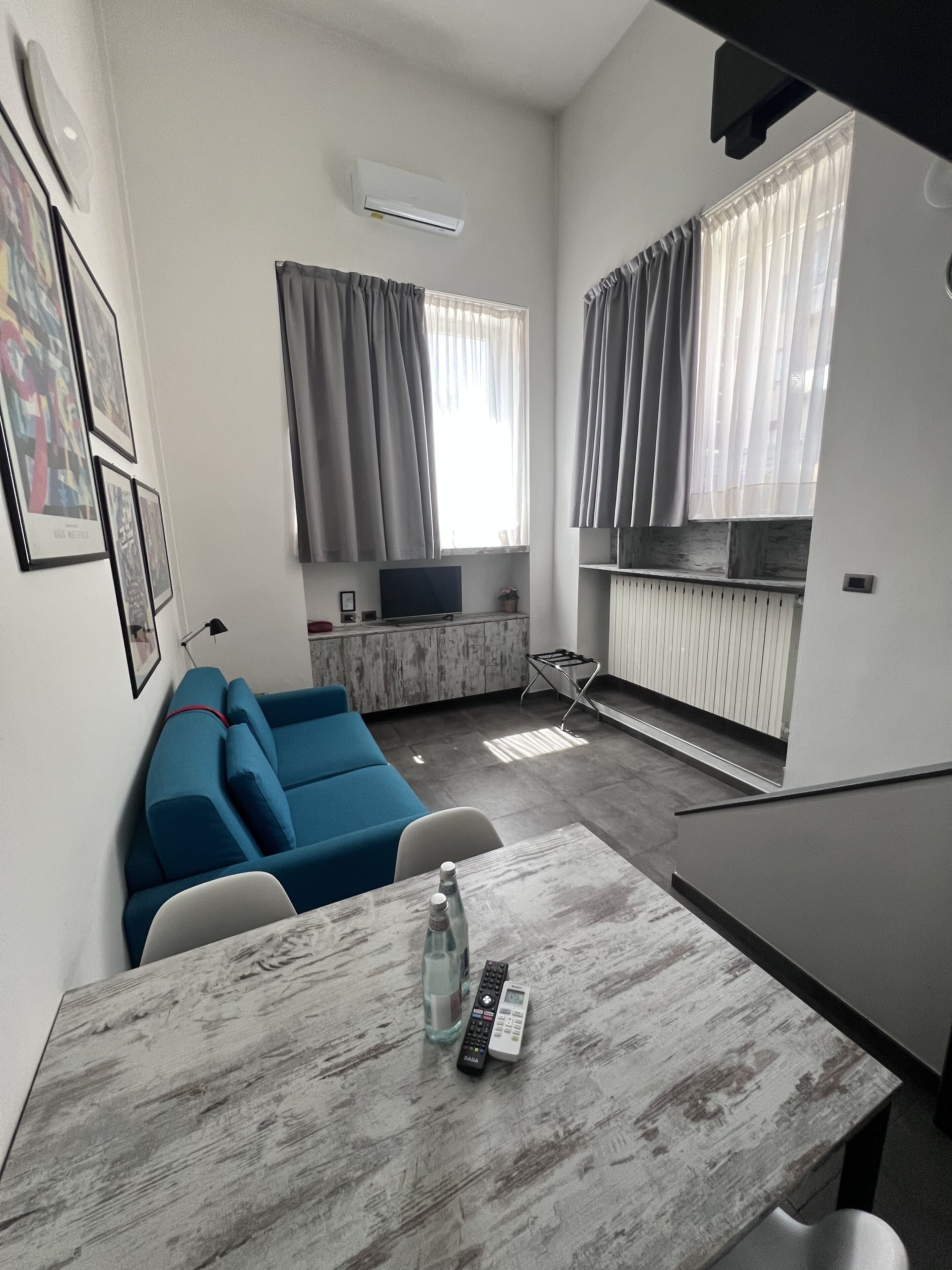 Un salón moderno con un sofá azul, una mesa de comedor con una botella y controles remotos, un televisor y una zona de cocina con un radiador.