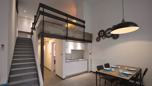 Una cocina moderna con armarios blancos, una mesa de comedor preparada para cuatro comensales y una escalera que sube a un nivel superior.