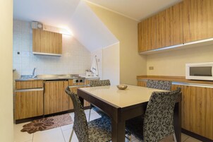 Una cocina compacta con armarios de madera, un microondas, un lavamanos y una mesa de comedor con sillas estampadas.