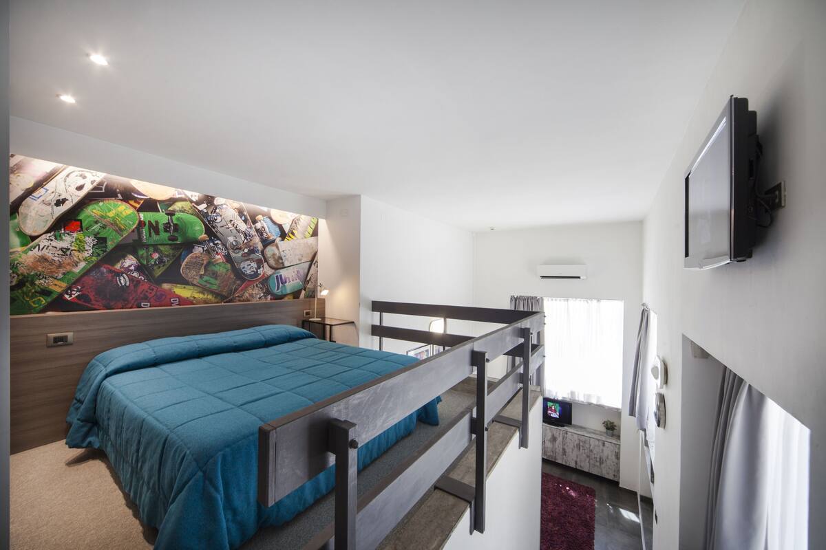 Une chambre avec un lit superposé, une fresque colorée sur le mur, une télévision et une fenêtre avec des rideaux.