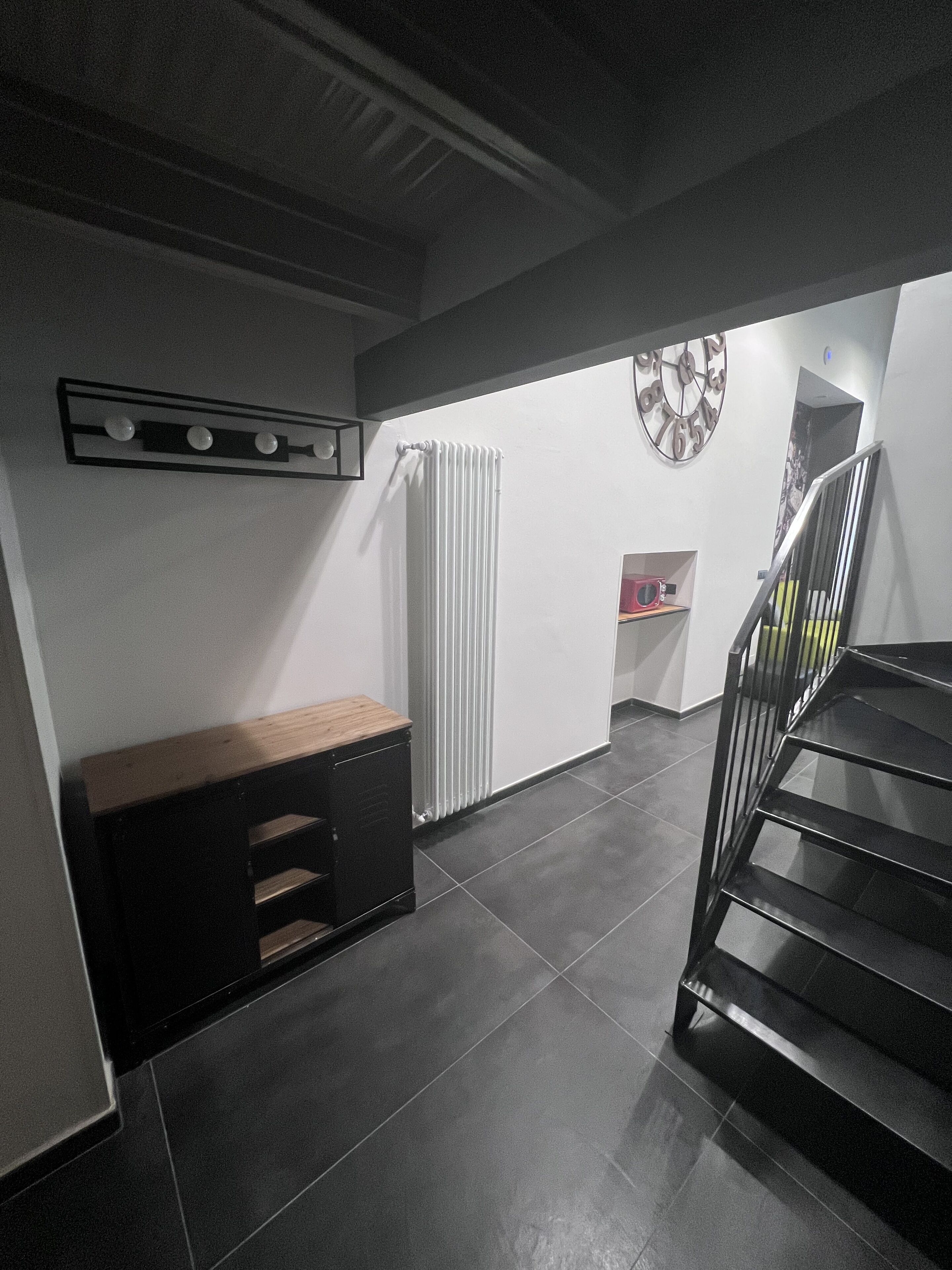 En modern hall med en trappa, ett element, ett träskåp och en klocka på väggen.