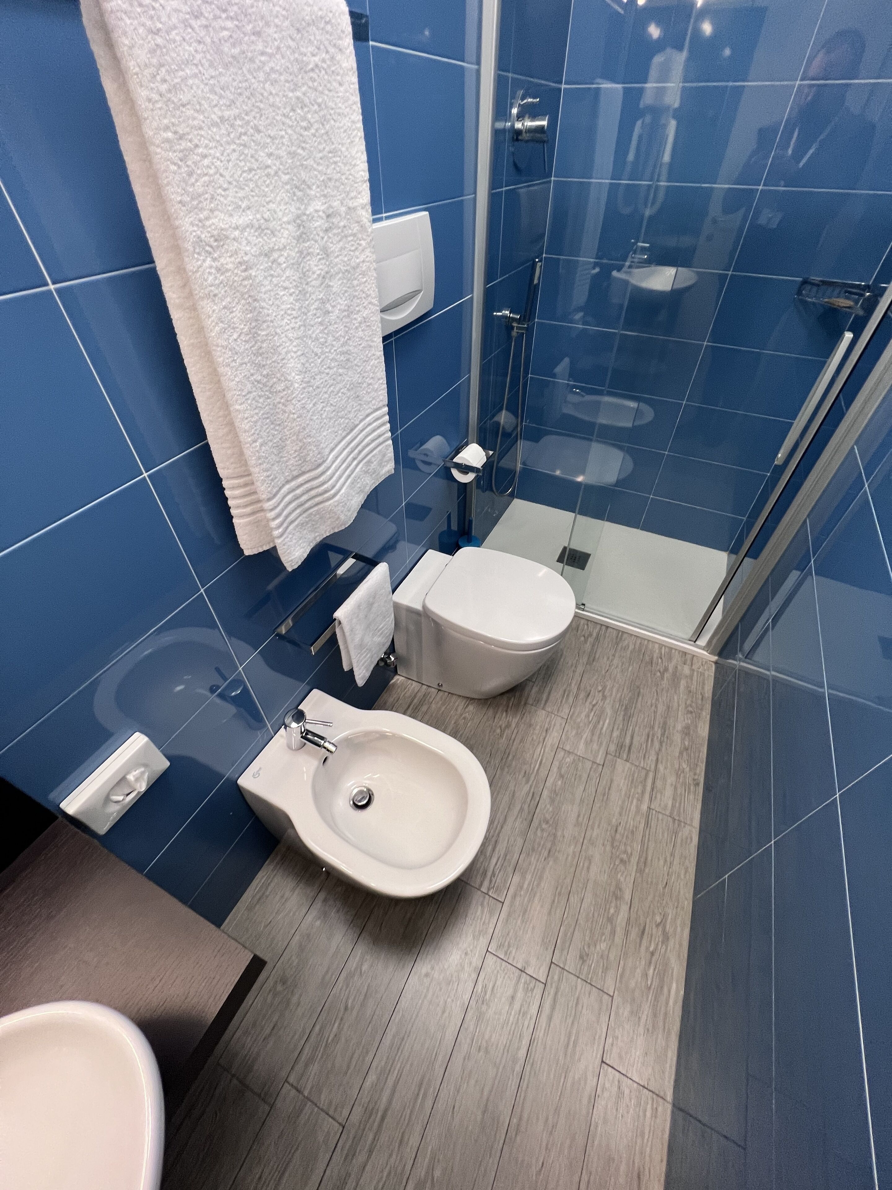 A modern bathroom with blue tiles, a white toilet, a bidet, and a sink.