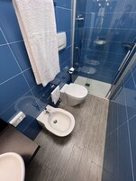 A modern bathroom with blue tiles, a white toilet, a bidet, and a sink.
