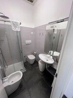 A modern bathroom with a glass-enclosed shower, a bidet, a sink, and a toilet.