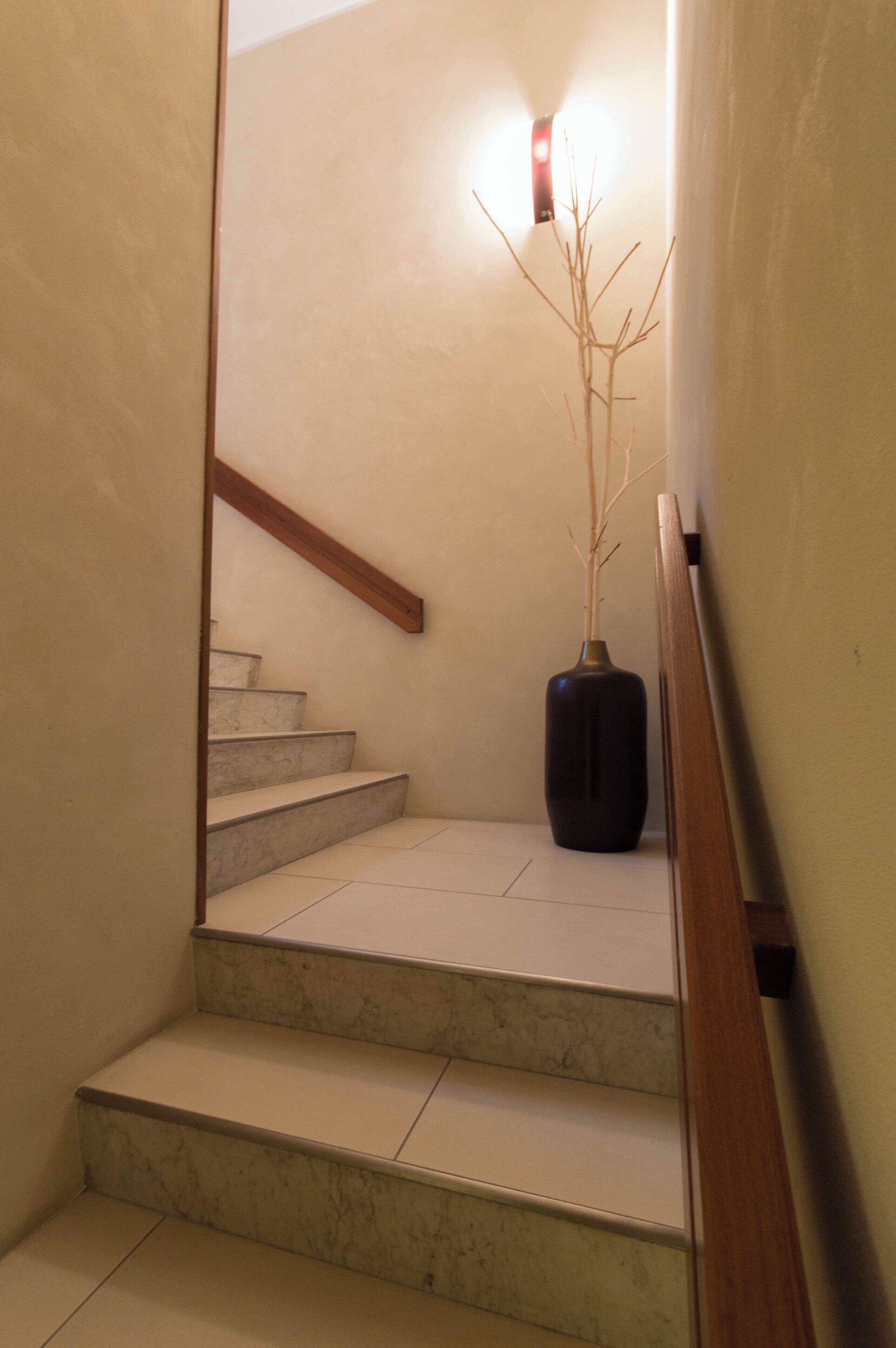 A staircase with a wooden handrail and a vase with branches on the landing.
