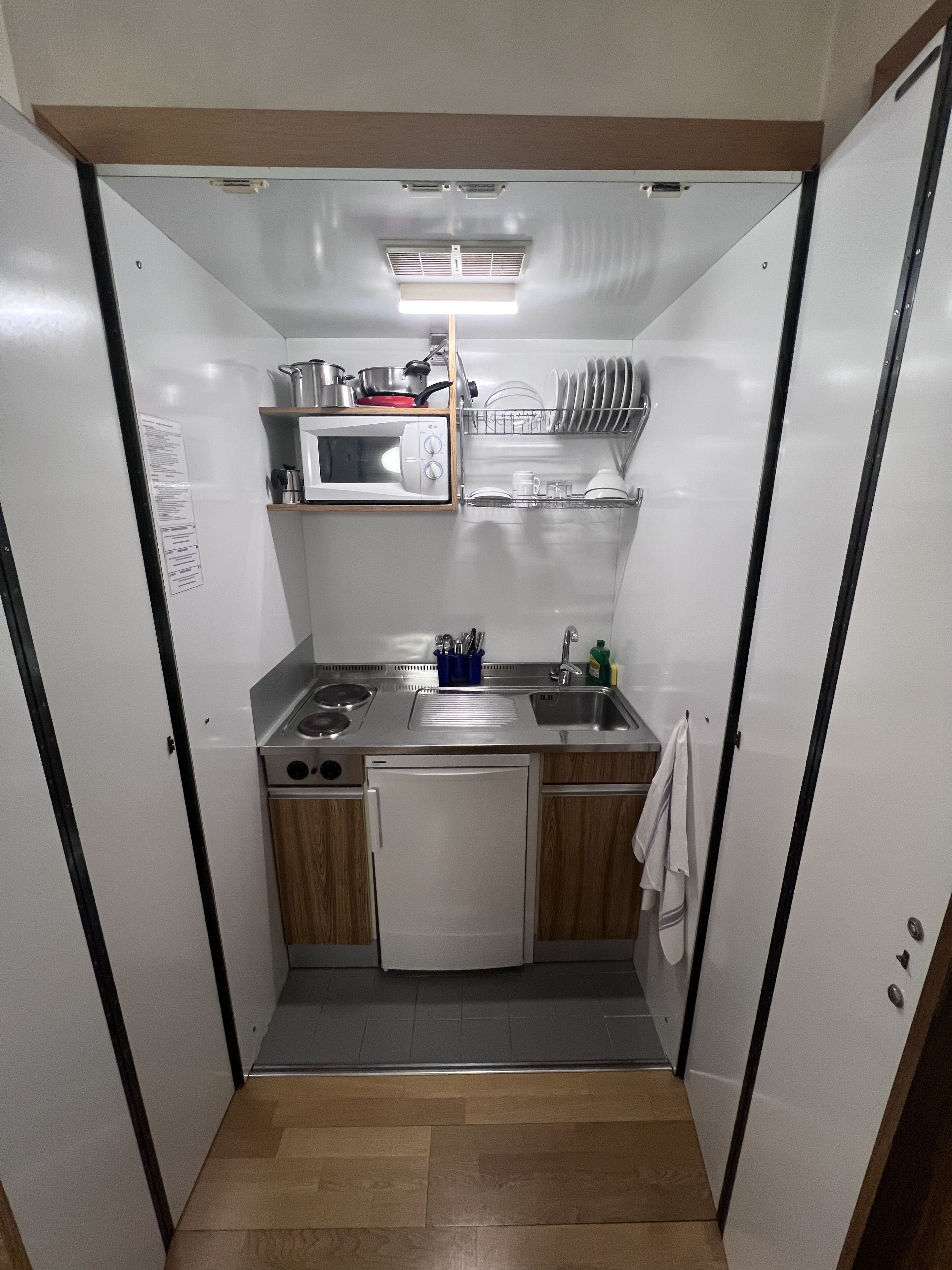 A compact kitchenette with a microwave, stove, sink, and dish rack.
