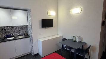 Een compacte kamer met een kitchenette, een bed, een televisie en twee wandlampen.