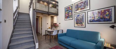 A modern living room with a blue sofa, a staircase, and a dining area.
