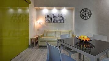 Un espace repas moderne avec une table en verre, des chaises, un canapé et une horloge murale.
