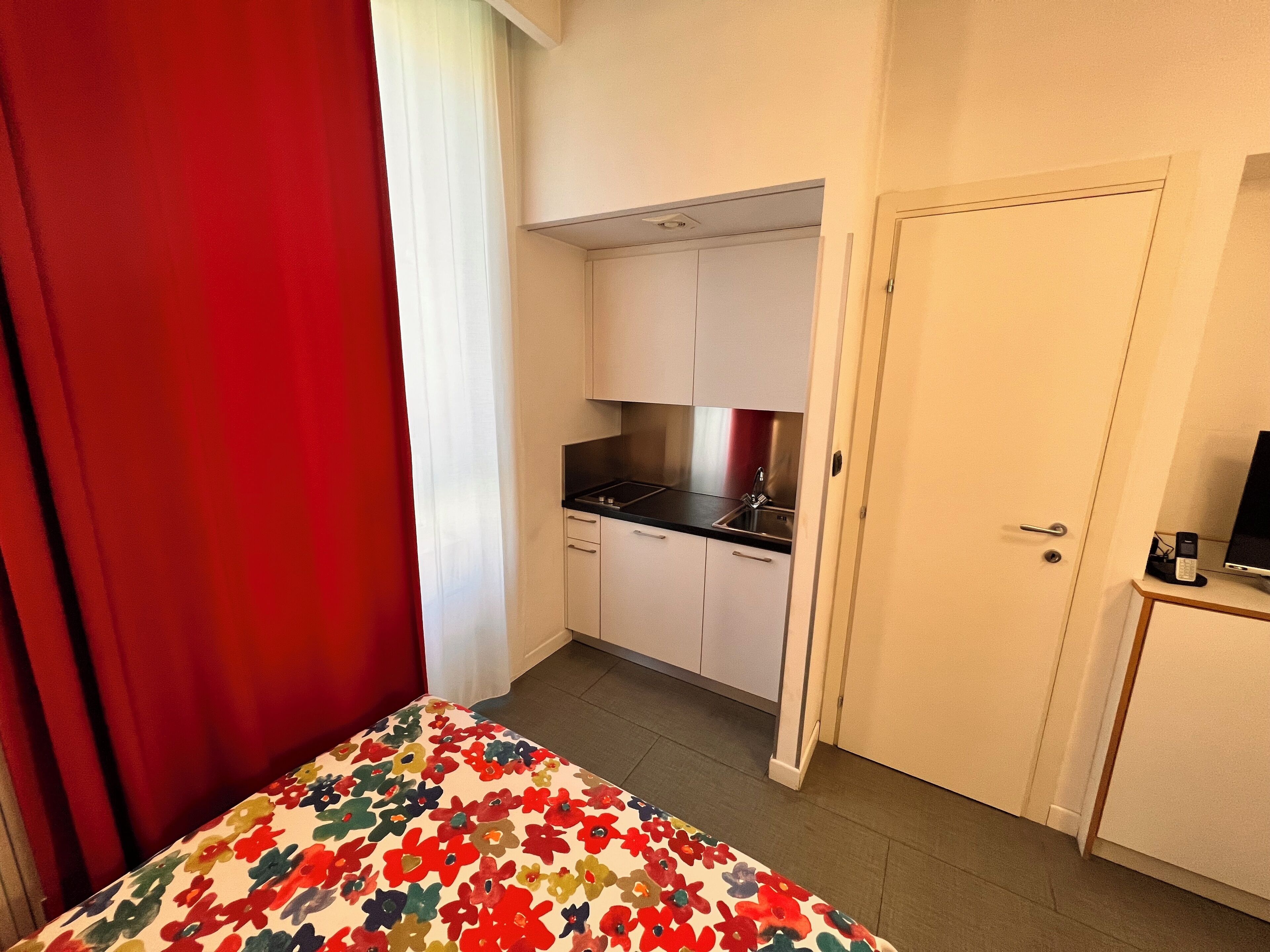 Pieni hotellihuone, jossa on sänky, pieni keittonurkkaus ja ovi, joka johtaa kylpyhuoneeseen.