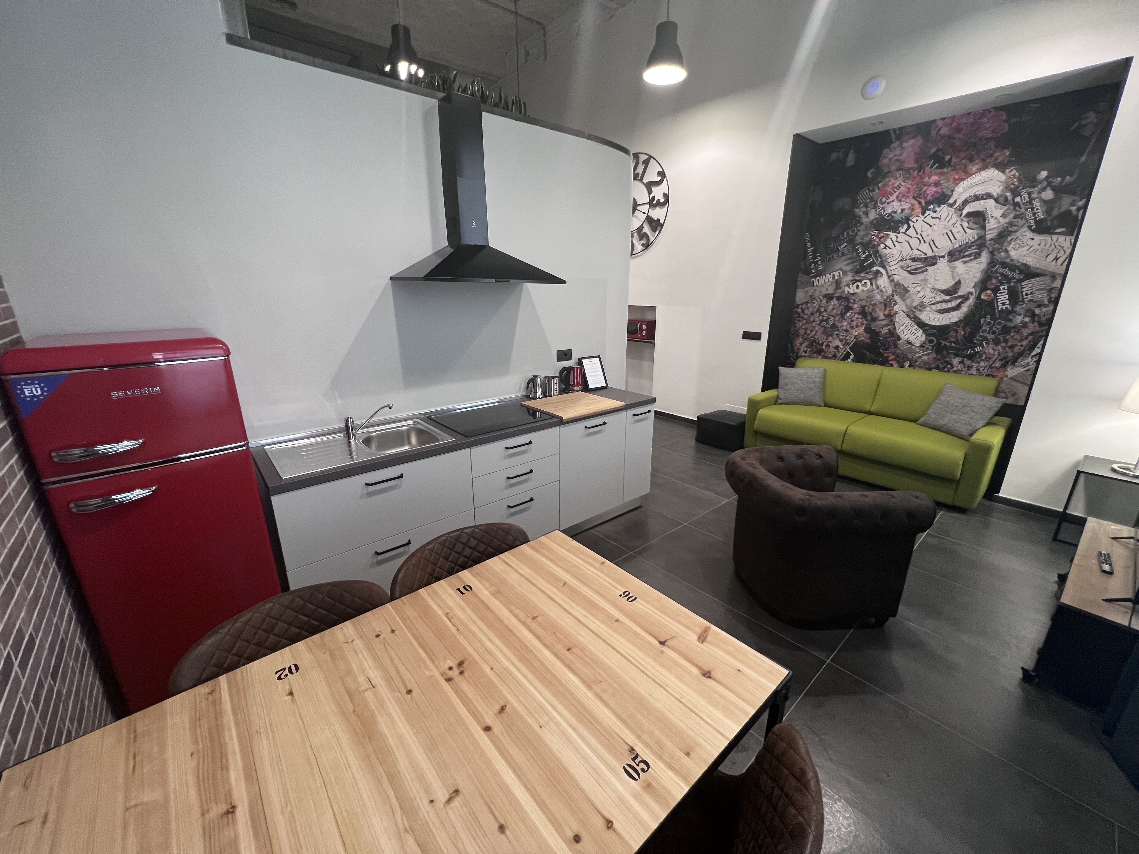 A modern kitchen with a red refrigerator, a wooden dining table, and a green sofa.