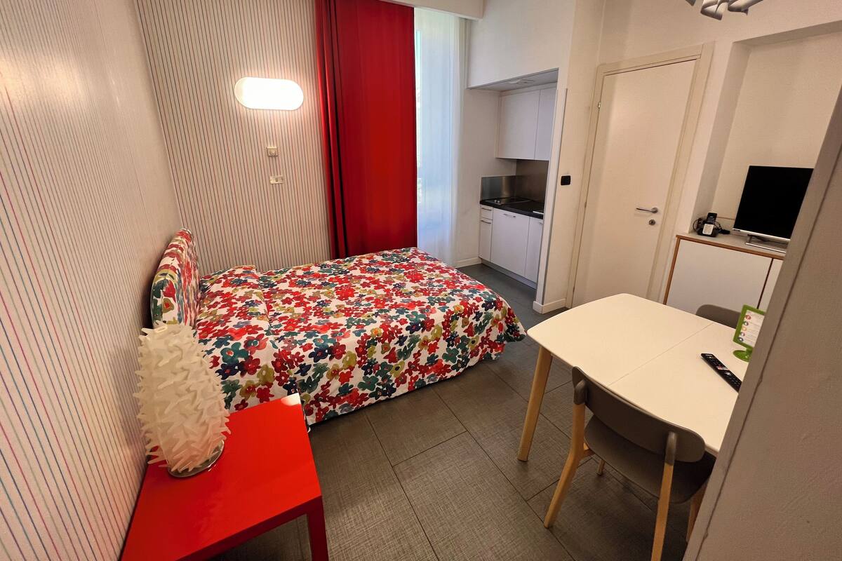 Une chambre d’hôtel compacte comprenant un lit, un petit bureau, une chaise, une kitchenette et un téléviseur.