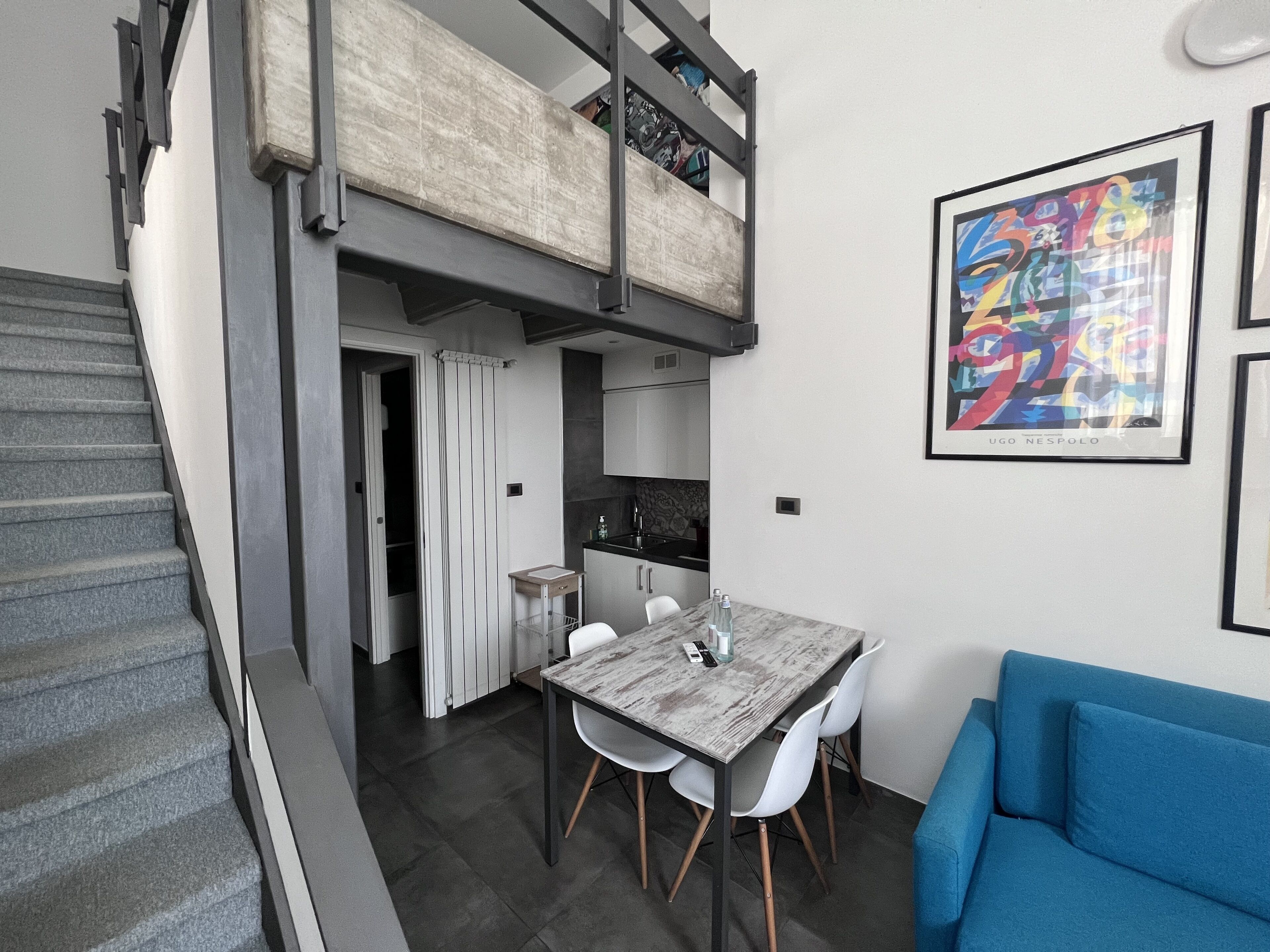 A modern apartment with a dining area, a blue sofa, and a staircase leading to a loft.