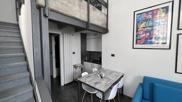 A modern apartment with a dining area, a blue sofa, and a staircase leading to a loft.