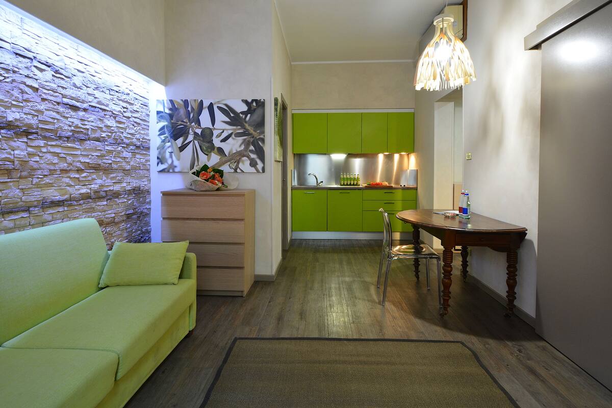 Un espace de vie compact comprenant un canapé vert, une table à manger et un coin cuisine avec des meubles de couleur verte.