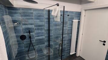 Une salle de bain moderne avec une douche à parois de verre, des murs recouverts de carreaux bleus, une porte blanche et un porte-serviettes visible.