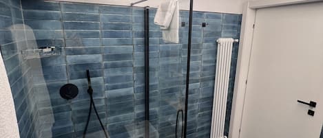 Une salle de bain moderne avec une douche à parois de verre, des murs recouverts de carreaux bleus, une porte blanche et un porte-serviettes visible.