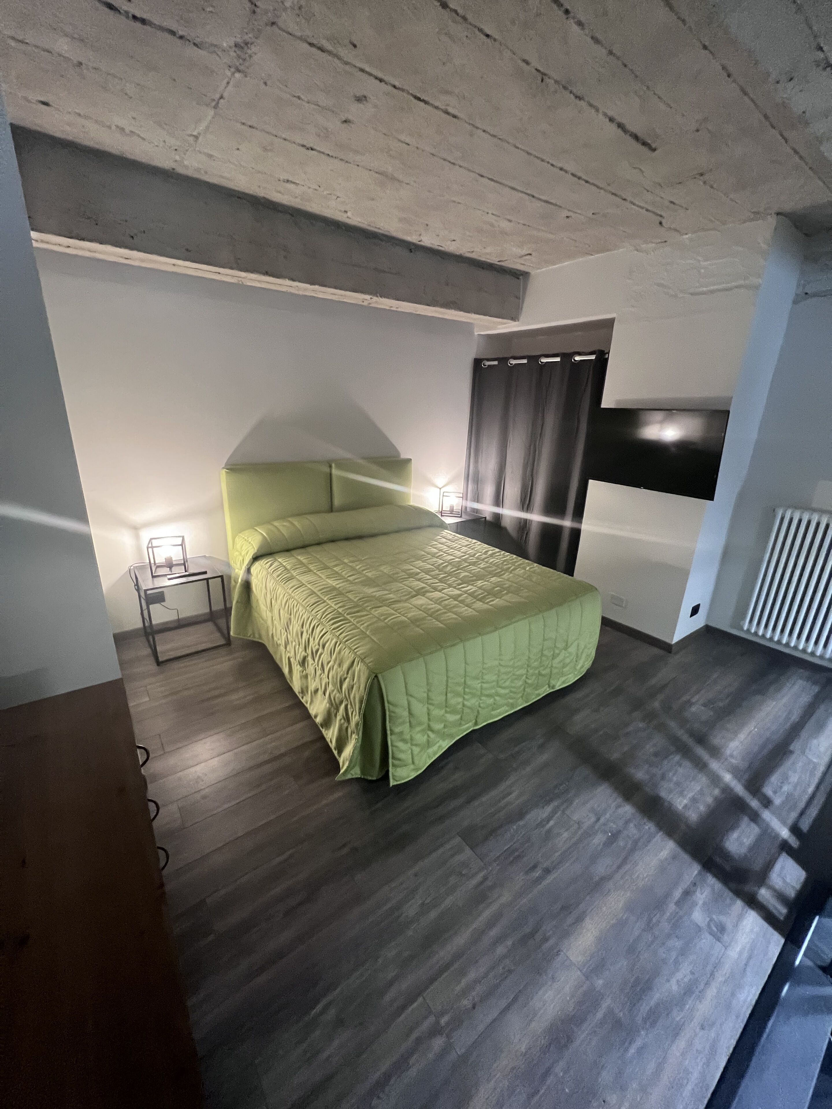 Ein Schlafzimmer mit Bett, Nachttisch, Lampe und einem Fenster mit Vorhängen.