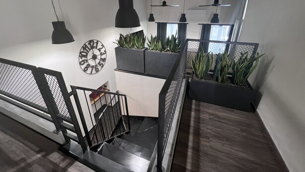 Una escalera moderna con barandales negros, un reloj de pared y plantas en macetas.