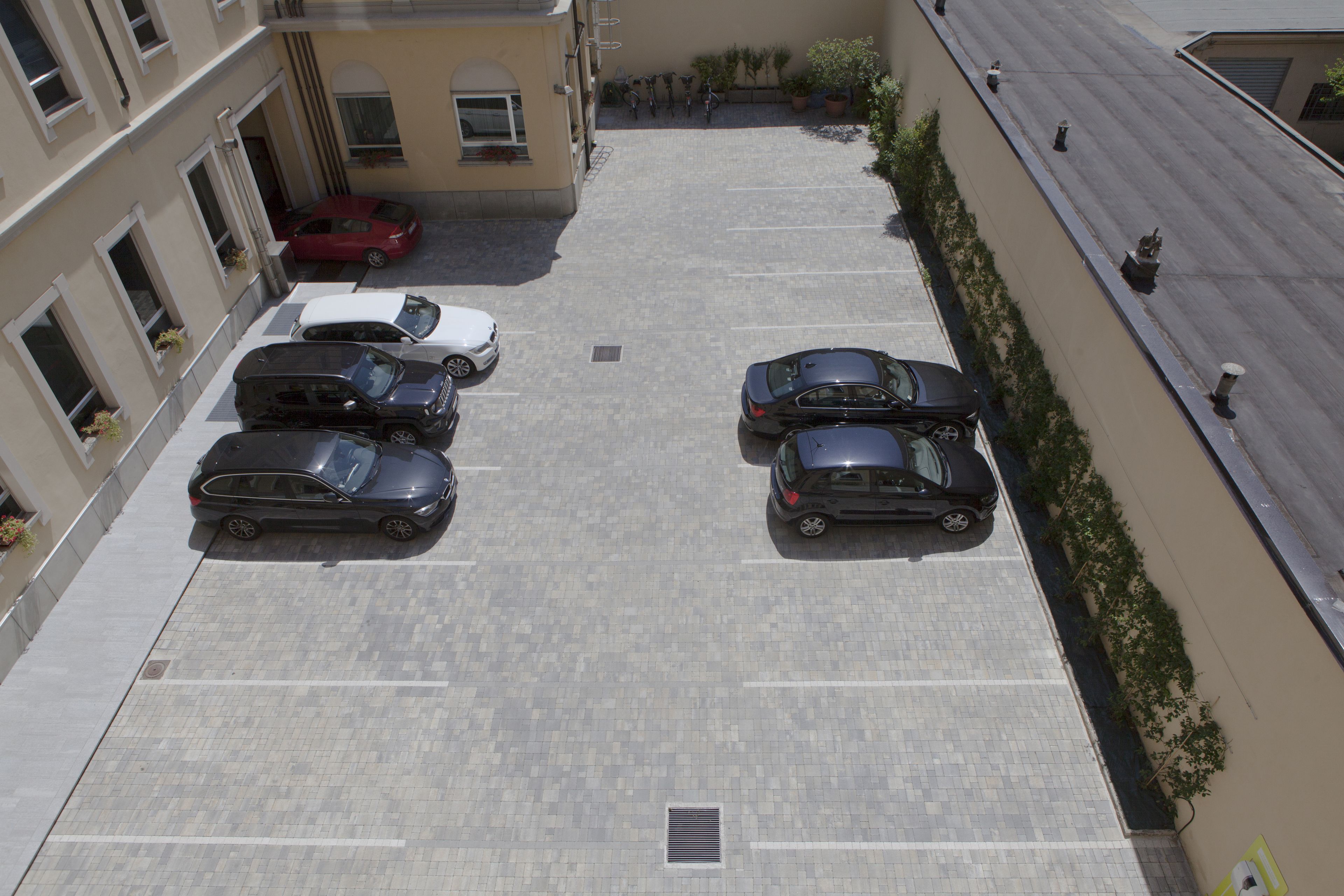 An aerial view of a parking lot with several cars parked, surrounded by buildings with balconies and potted plants.