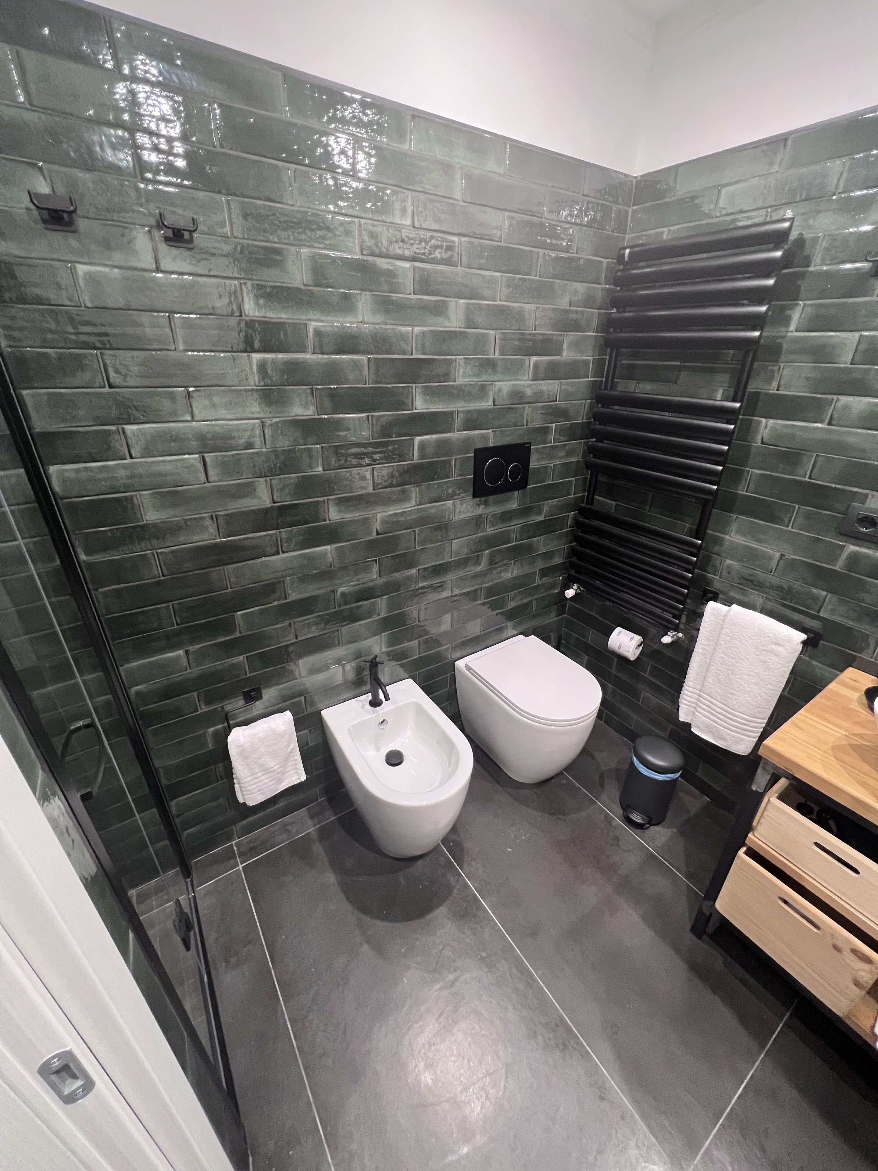 A modern bathroom with a brick wall, a bidet, a toilet, a towel rack, and a wooden vanity.