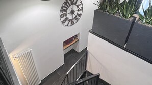 Una escalera con barandilla negra, un reloj fijado a la pared y una planta en maceta.