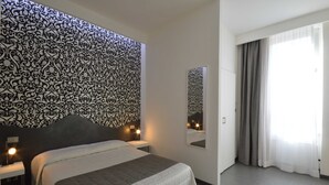 Habitación de hotel con una cama grande, mesitas de noche con lámparas, un papel tapiz decorado, un espejo y un ventanal con cortinas.