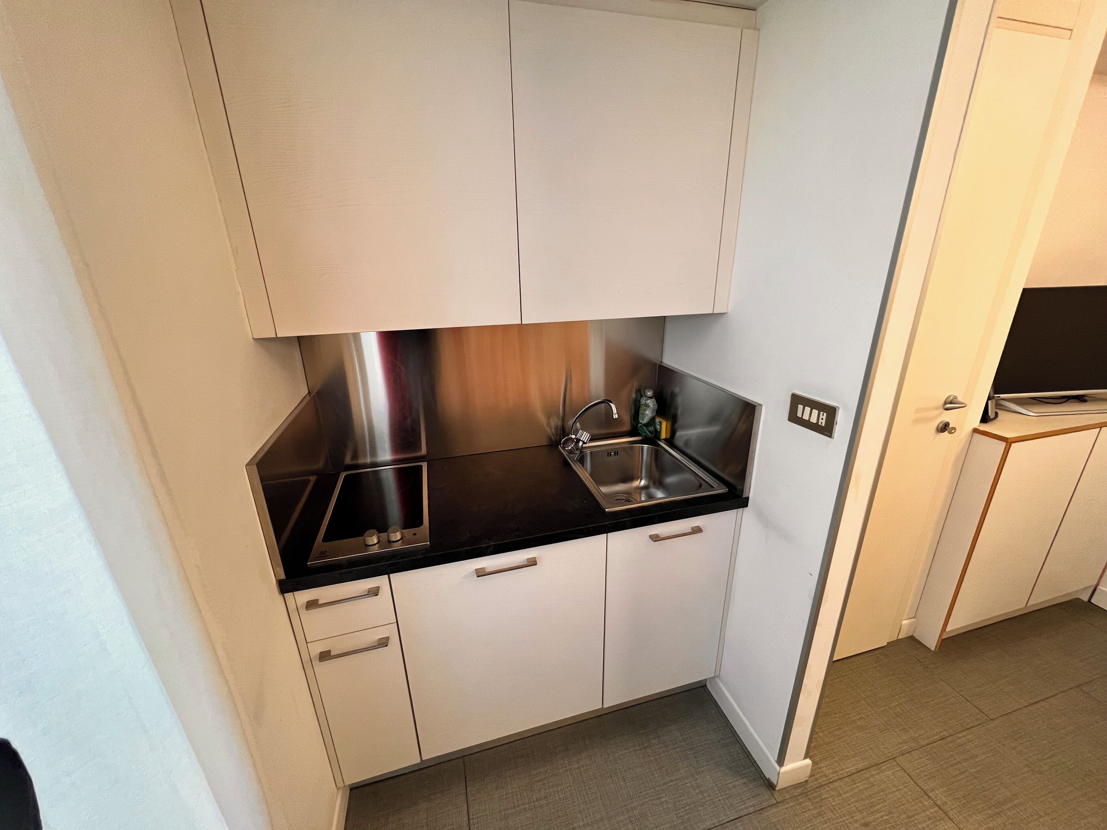 A compact kitchen with white cabinets, a black countertop, stainless steel appliances, and a built-in sink.