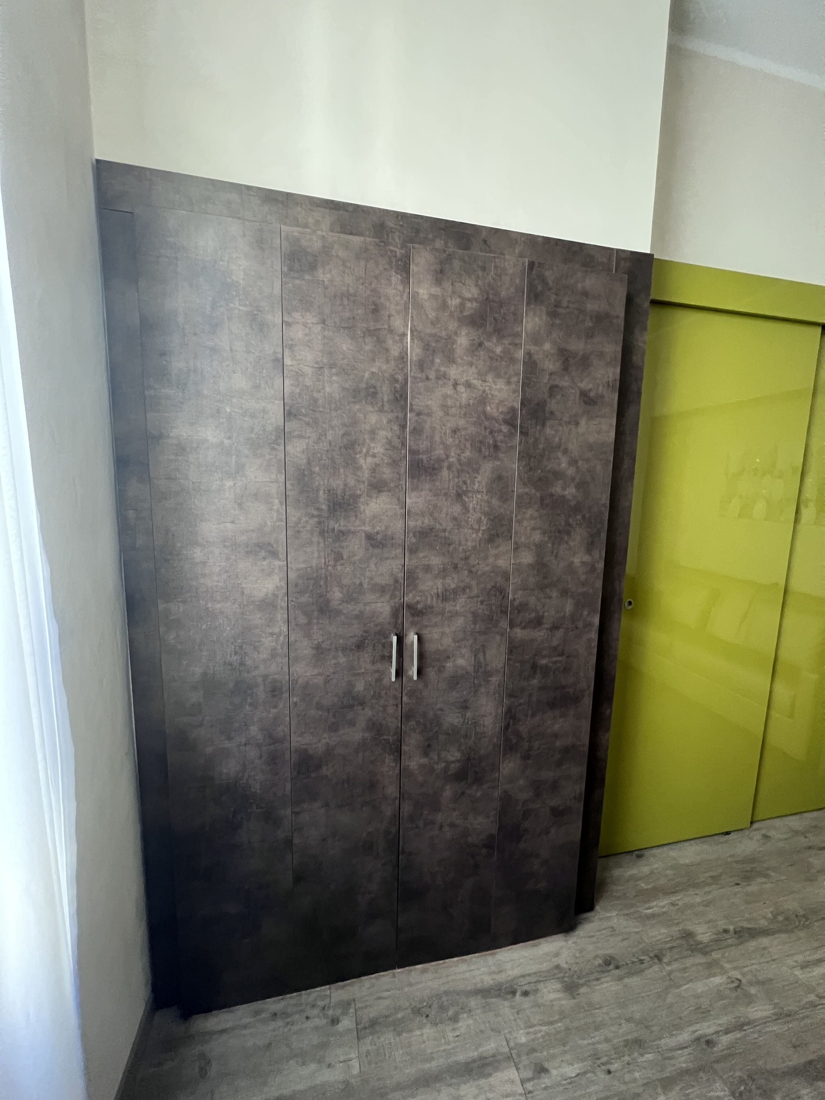 A large wardrobe with two handles, a green door, and a grey floor.