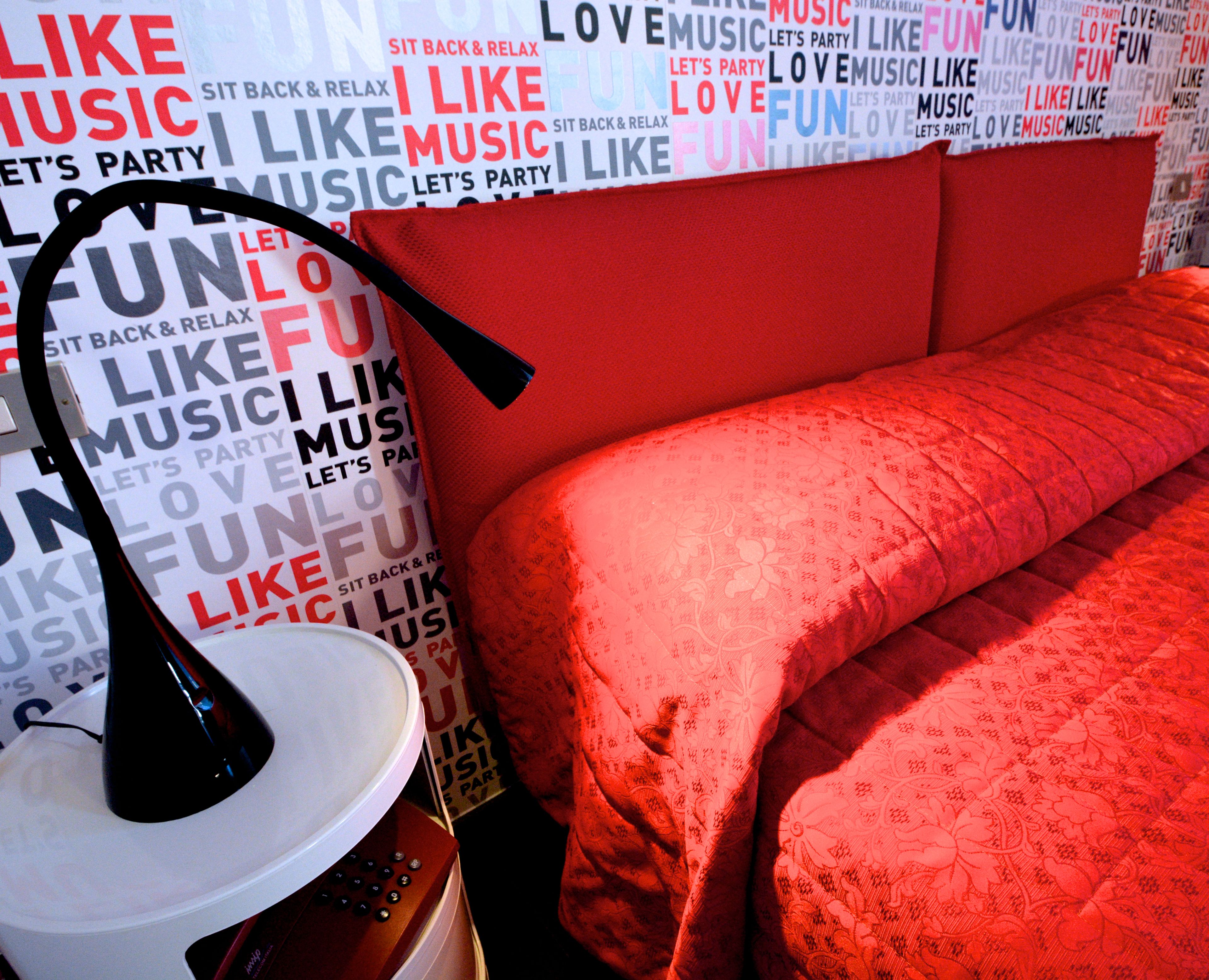 A room with a red headboard, a white lamp, and a bed with a red bedspread.