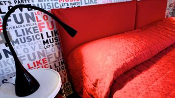 Una habitación con cabecera roja, lámpara blanca y cama con colcha roja.