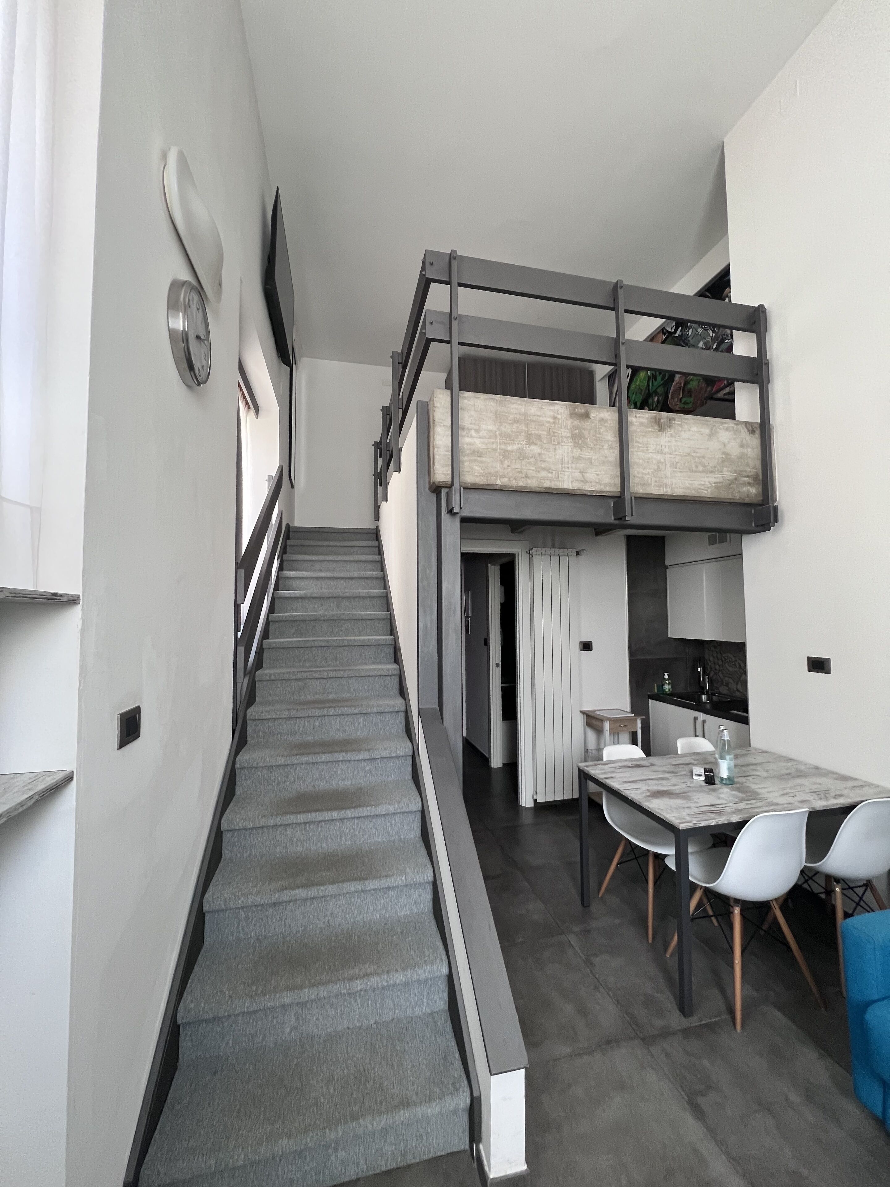 A modern interior with a staircase leading to a lofted sleeping area, a dining table with chairs, and a kitchen area.