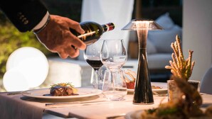 A dining table with a bottle of wine being poured into a glass, surrounded by empty wine glasses and a decorative lamp. - Enjoy Garda Hotel (Peschiera del Garda)