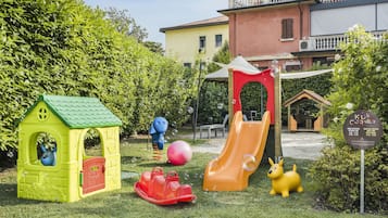 Children can play and explore in this designated play area surrounded by lush greenery and a nearby building.