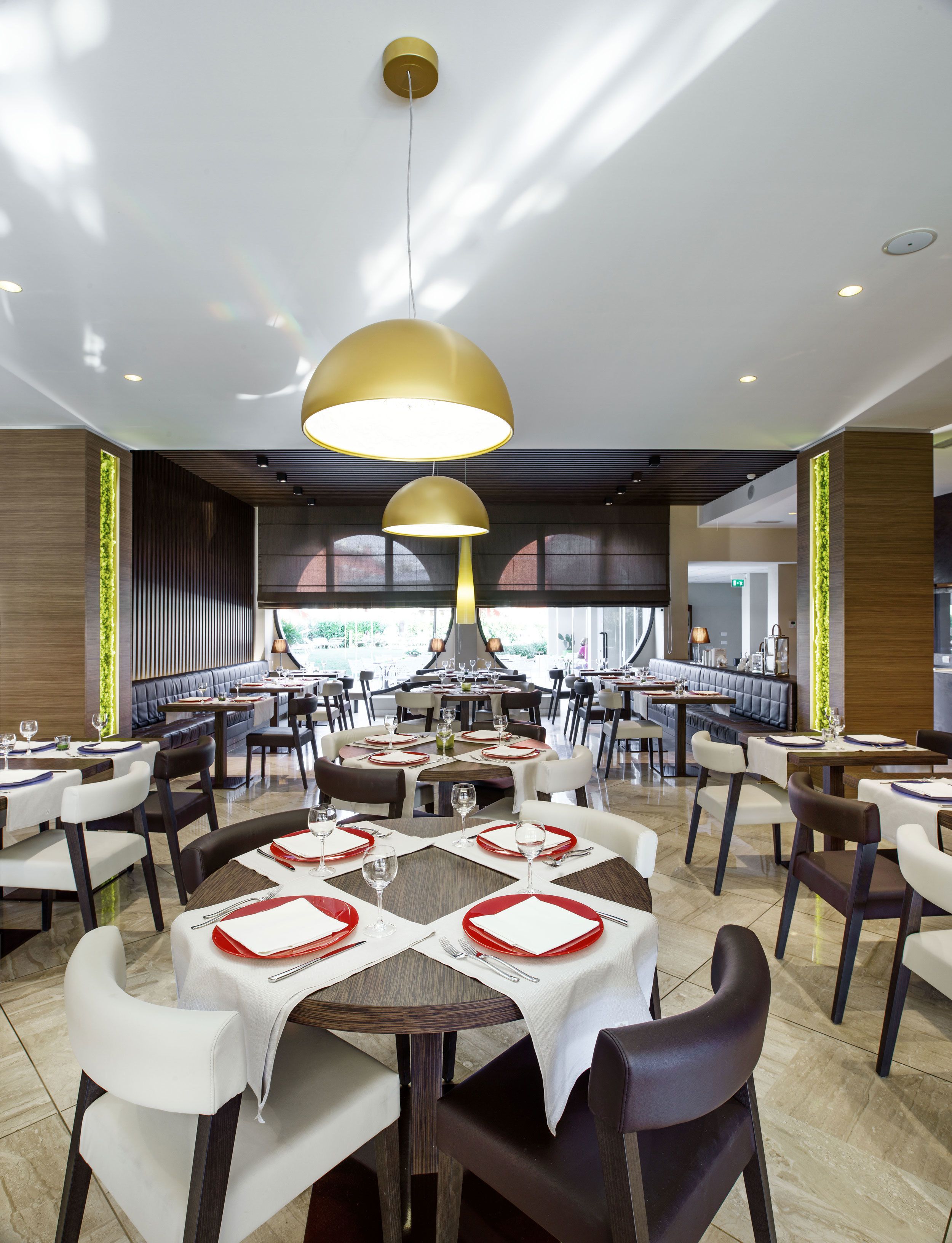 Ein modernes Restaurant mit runden Tischen, weißen und braunen Stühlen und einer großen Pendelleuchte.