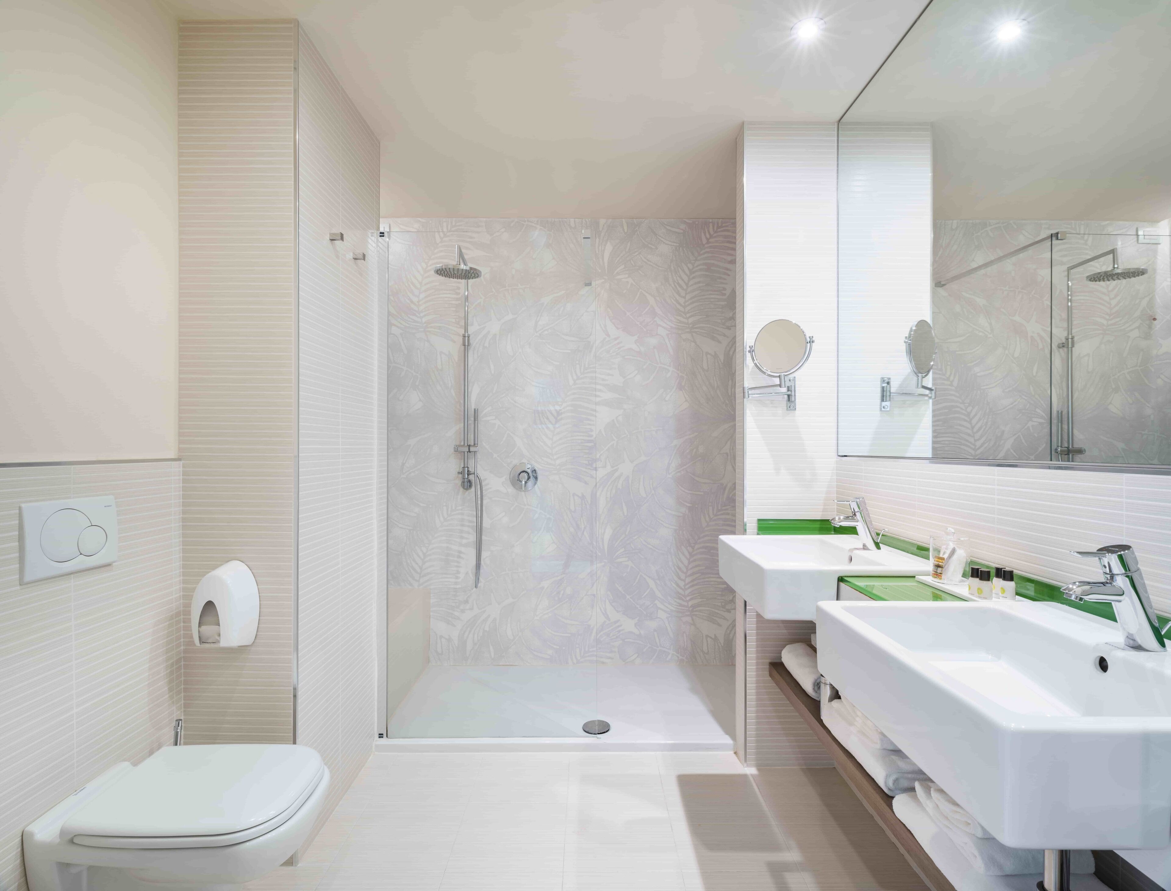 Une salle de bain moderne avec une douche à parois de verre, deux lavabos, des toilettes et un miroir.