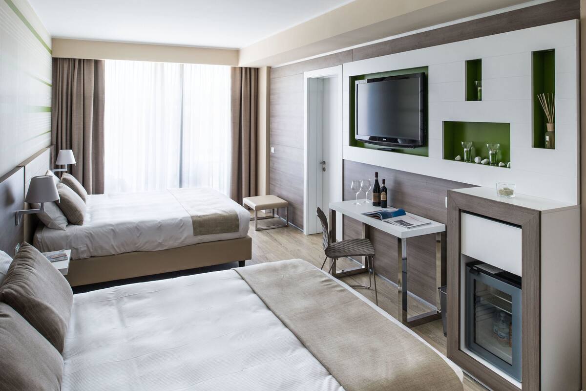 A hotel room with two beds, a desk, a TV, and a minibar.