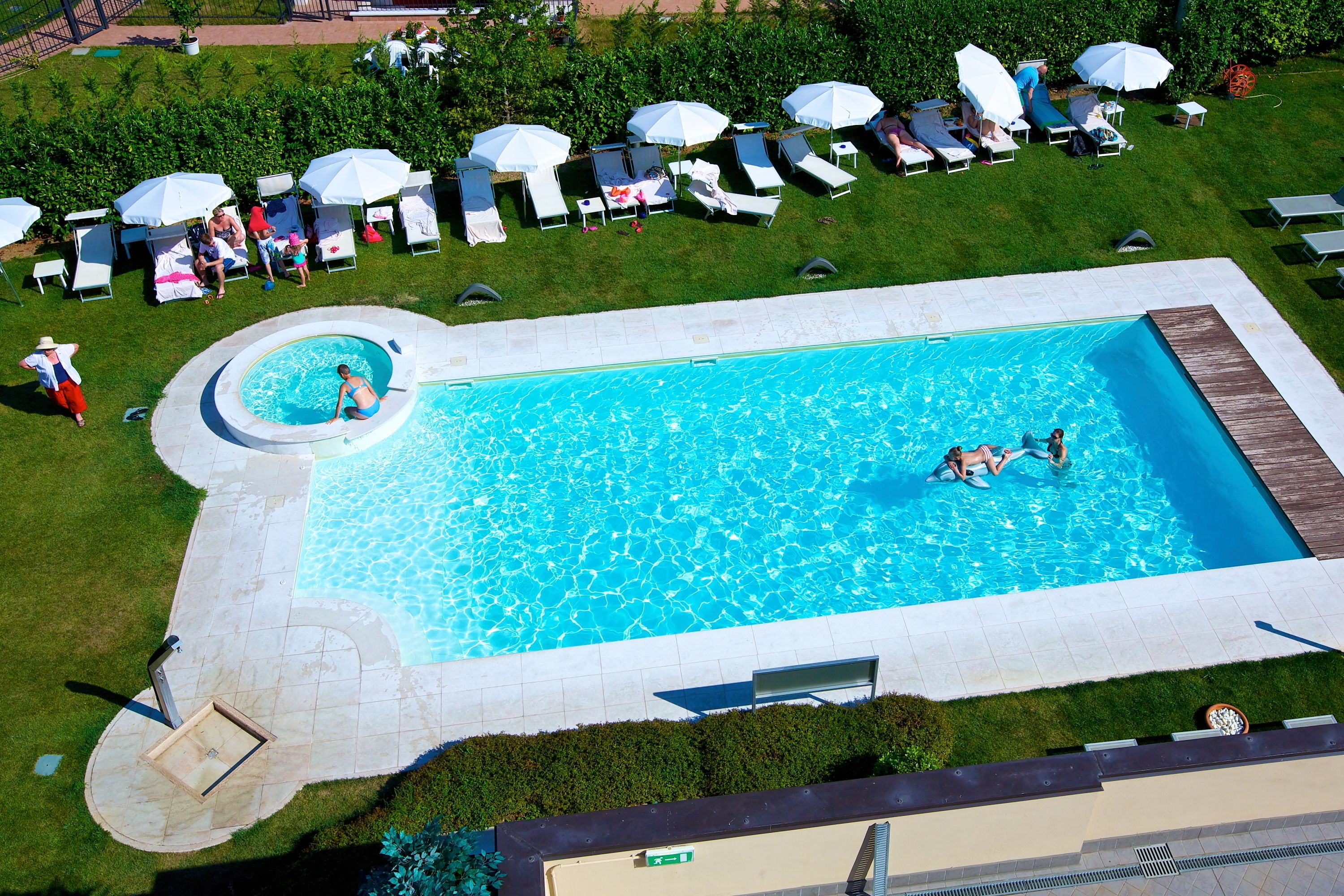 A large rectangular swimming pool with a circular hot tub, surrounded by lounge chairs and umbrellas.