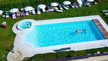 A large rectangular swimming pool with a circular hot tub, surrounded by lounge chairs and umbrellas.