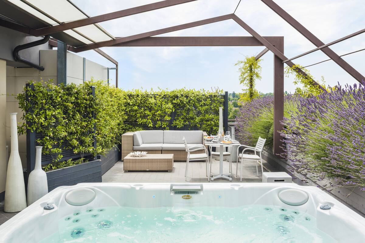 A rooftop patio with a hot tub, seating area, and lush greenery.